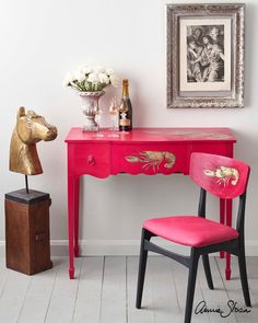 a pink desk with two chairs next to it and a painting on the wall behind it