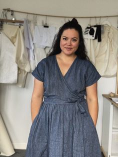 a woman in a blue dress standing next to clothes hanging on a rack and looking at the camera