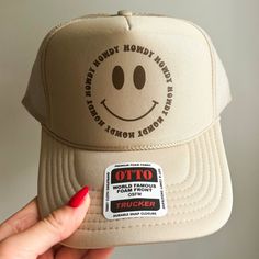 The perfect hat for beach days and country concerts alike! This hat is comprised of an Otto brand foam trucker hat in color khaki with a brown howdy smiley face design. Trendy Brown Summer Trucker Hat, Trendy Adjustable Beige Trucker Hat, Trendy Beige Trucker Hat, One Size Fits Most, Trendy Beige Trucker Hat One Size Fits Most, Trendy Beige Trucker Hat Baseball Cap, Trendy Beige Snapback Trucker Hat, Trendy Brown Trucker Hat For The Beach, Brown Flat Brim Trucker Hat For Summer, Trendy Beige Trucker Hat