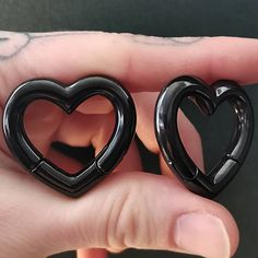 two black heart shaped earrings are held in the palm