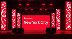 the new york city sign is lit up in red and white with black stands on either side