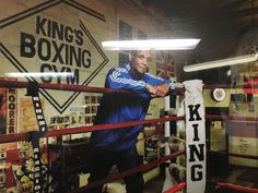 a man standing next to a boxing ring holding a punching glove in front of a king's boxing club sign