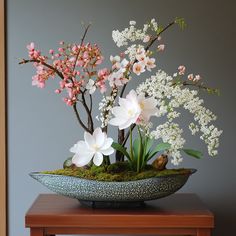 an arrangement of flowers is displayed in a bowl on a table with moss and rocks