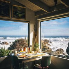 there is a desk with books on it in front of two windows overlooking the ocean