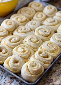 a pan filled with cinnamon rolls sitting on top of a counter next to a yellow bowl