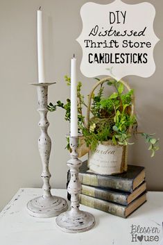 two white candlesticks sitting on top of books next to a basket with plants