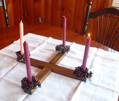 four candles are placed in the middle of a cross on a table with white linens