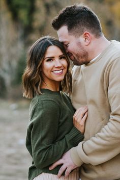 a man and woman hugging each other in front of trees