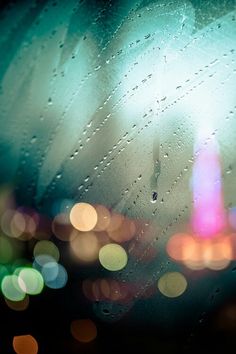 rain drops on the windshield of a car as traffic lights are blurred in the background