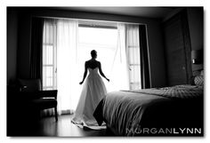 a woman standing in front of a window next to a bed