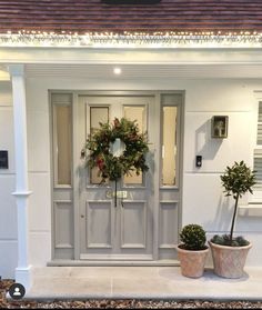 two potted plants are sitting in front of the door to a white house with a wreath on it