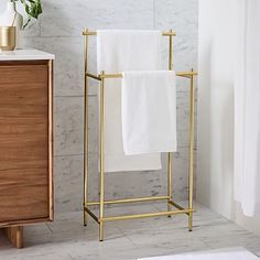 two white towels are hanging on a gold towel rack next to a marble wall and floor