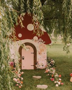 a mushroom shaped house with flowers around it and a pink door in the grass under a tree