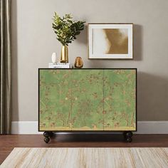 a green cabinet sitting on top of a hard wood floor next to a painting and potted plant