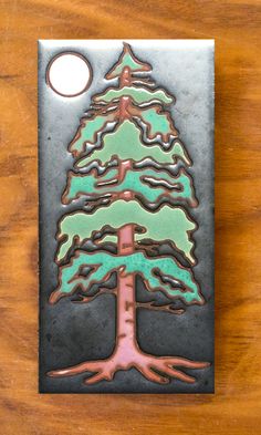 a metal plaque with a green and pink christmas tree on it's side, sitting on a wooden table