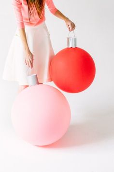 a woman is standing next to a large red ball and a pink ornament