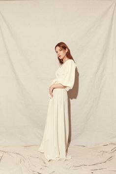 a woman is standing in front of a white backdrop wearing a long dress and heels