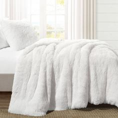 a white bed with a fluffy blanket on top of it and pillows in the background