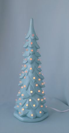 a blue ceramic christmas tree with lights on it's base and a white cord