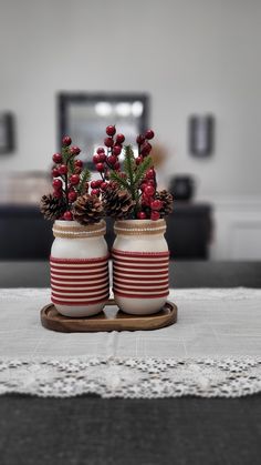 two red and white striped vases with pine cones on the top are sitting on a table