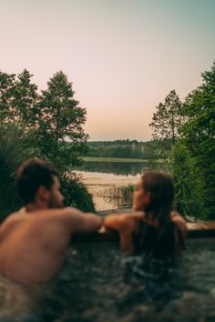 two people sitting in a hot tub looking out at the water and trees around them