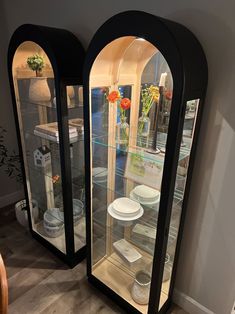 two glass display cases with plates and vases on them in the corner of a room