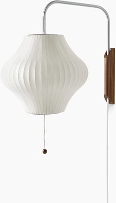 a white lamp hanging from a wall next to a wooden light fixture on a metal pole