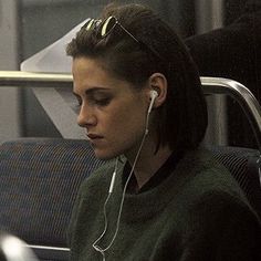 a woman sitting on a bus with headphones in her ears and looking at her cell phone