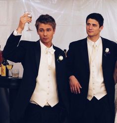 two men in tuxedos standing next to each other with wine glasses on their shoulders