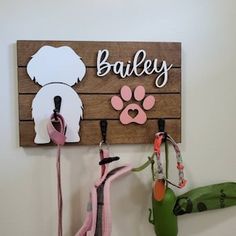 there is a dog leash holder on the wall next to some key hooks and a sign that says bailey