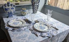 a table set for two with blue and white china on it, in front of a window