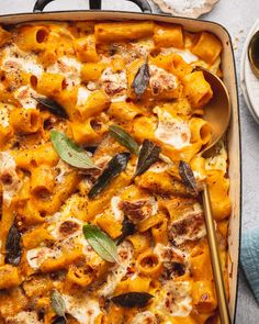 a casserole dish with pasta, cheese and sage leaves on the side next to a cup of coffee