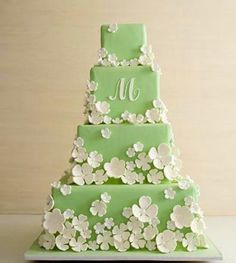 a three tiered green cake with white flowers on the bottom and monogrammed letters