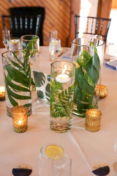 the table is set with candles and glass vases filled with water, greenery, and gold rimmed glasses