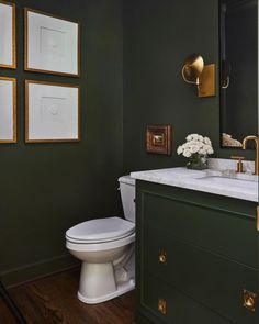 a white toilet sitting next to a bathroom sink under three framed pictures on the wall