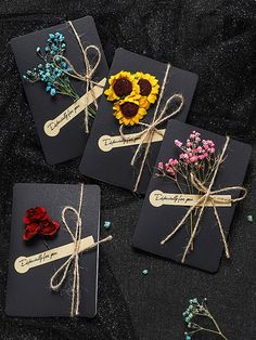 four cards with flowers tied to them on a black tablecloth covered surface, one has a tag that says congratulations and the other is decorated with twine