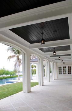 an outdoor covered patio with white columns and black ceiling lights on either side of the pool