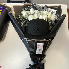 a bouquet of white roses in a black hat on top of a table next to chocolates