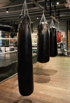 three black boxing bags hanging from the ceiling in a gym with wooden floors and hard wood flooring