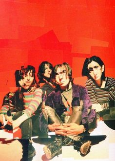 four young men sitting on the ground in front of a red wall