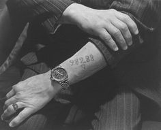 a man with a wrist tattoo on his left arm, sitting down and looking at the camera