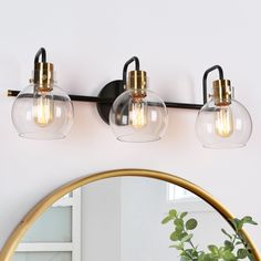 three light bathroom fixture with clear glass globes and gold accents on the wall next to a mirror