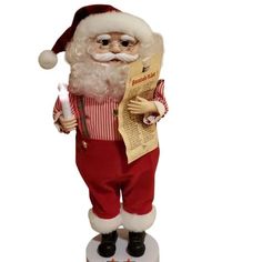 a statue of santa holding a newspaper and looking at it's right side while standing on a white surface