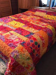 a bed with a colorful bedspread on top of it and drawers in the background