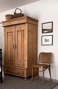 a wooden armoire in a bedroom next to a chair and pictures on the wall