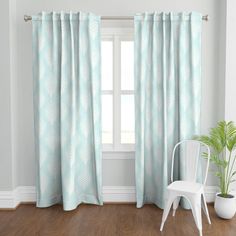 a white chair sitting in front of a window next to a green flowered curtain