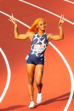 a woman running on a track with her arms in the air and one hand up