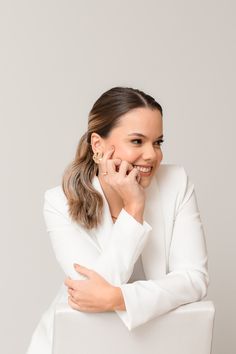 a woman sitting in a white chair with her hand on her chin and smiling at the camera