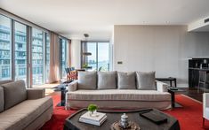 a living room filled with furniture next to large windows on top of a red rug