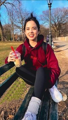 a woman sitting on a park bench with a drink in her hand and smiling at the camera